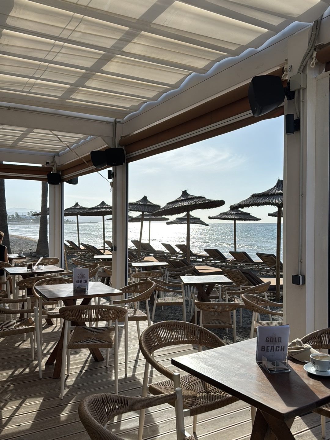 Interior de la terraza de Solo Beach al atardecer, con mesas de madera y vistas al mar
